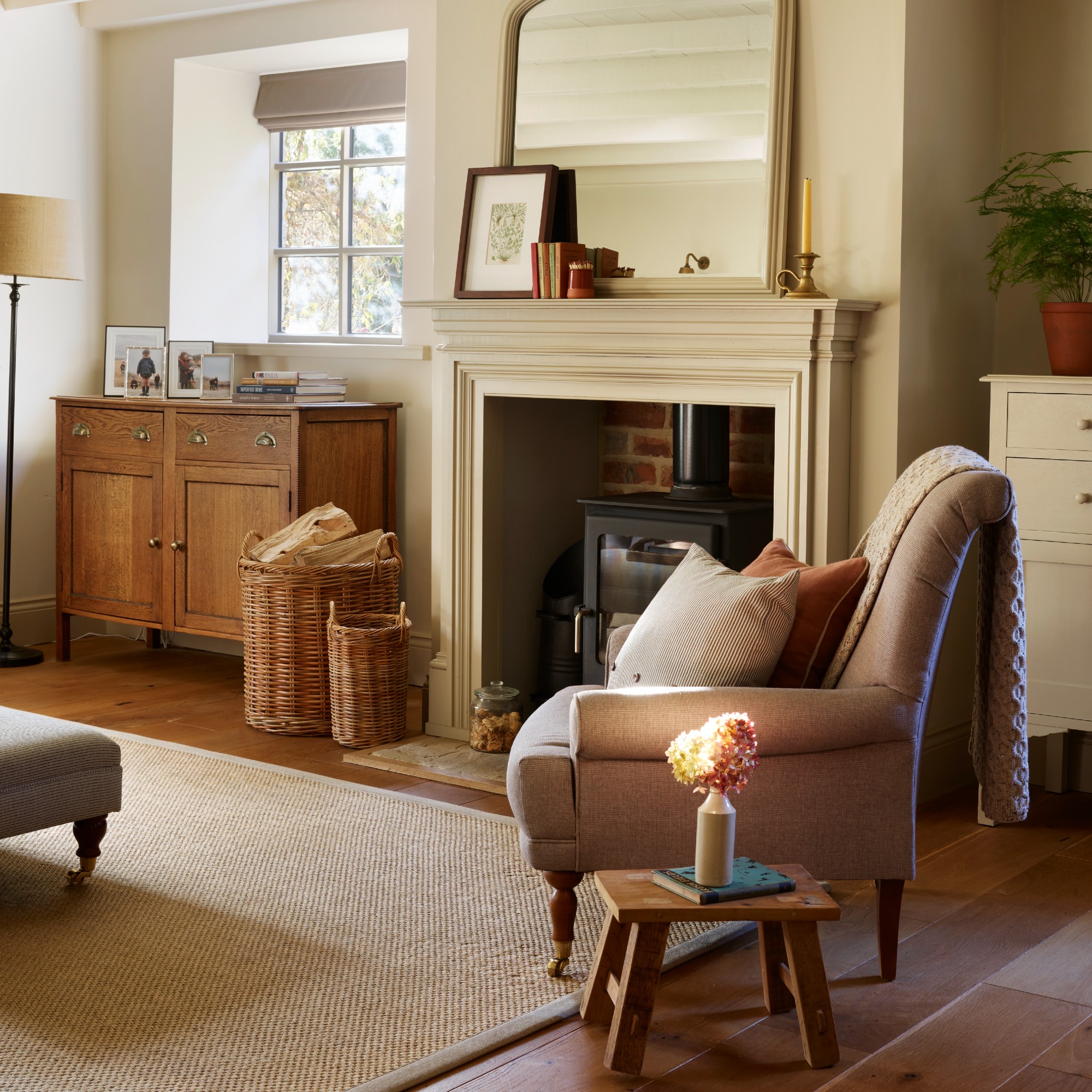 A neutral rustic living room with a wood-burning stove in a fireplace and a large mirror on the mantelpiece