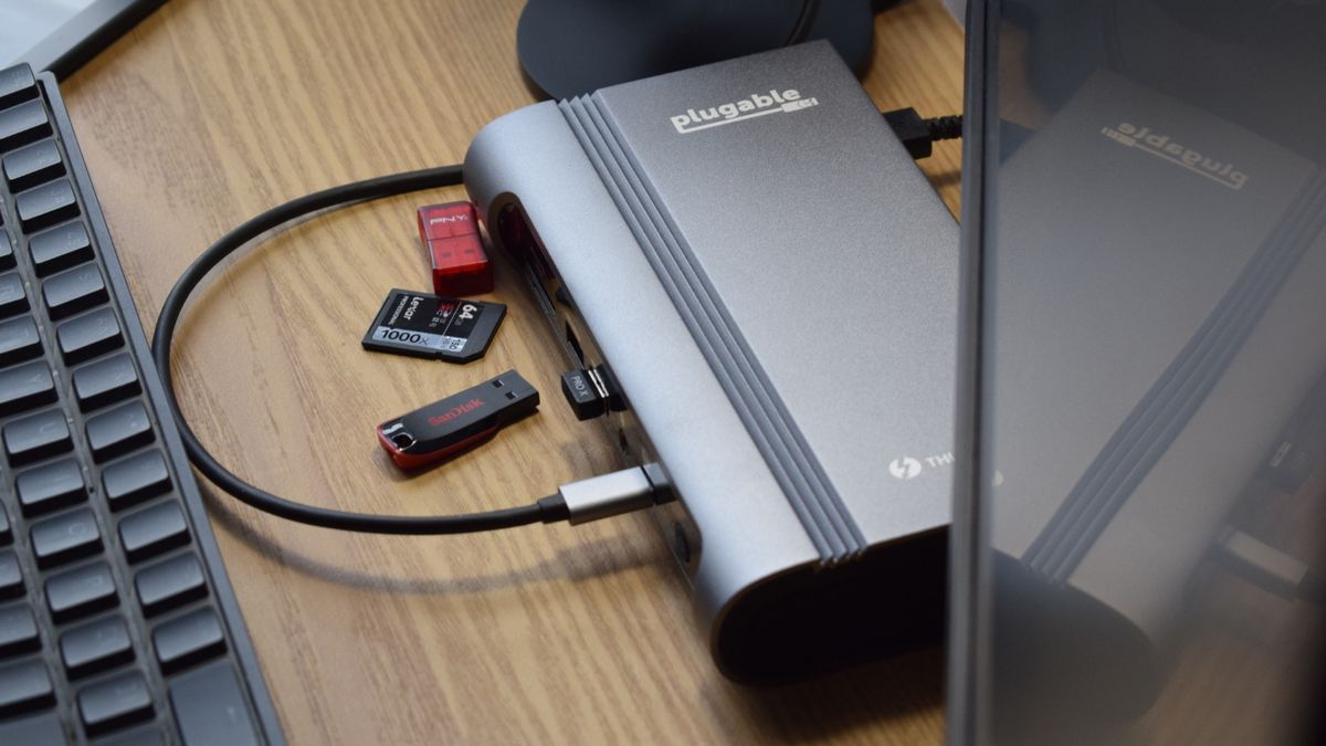 Photo of the Plugable Thunderbolt 4 &amp; USB4 Quad Display Docking Station (TBT4-UDZ) from above, showing the Plugable and Thunderbolt branding with various USB sticks and memory cards.