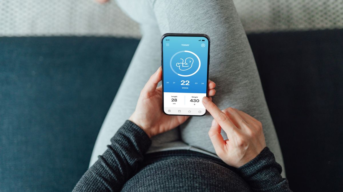 A point-of-view shot of a pregnant woman, holding a phone with an app that shows she is 22 weeks pregnant