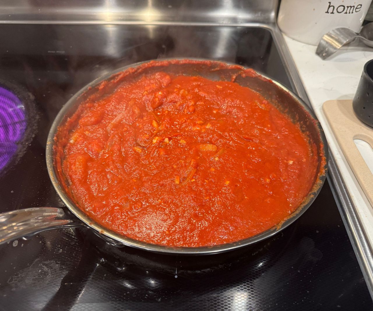 The Hestan NanoBond Skillet on a black stovetop, full of red pasta sauce