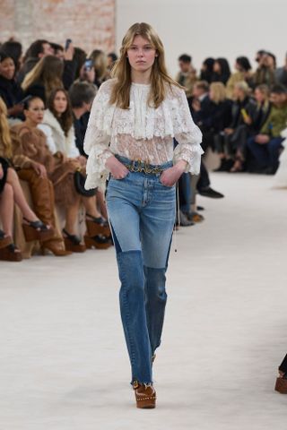 A Chloé model wearing a white lace blouse with jeans and clogs at the F/W 24 show.