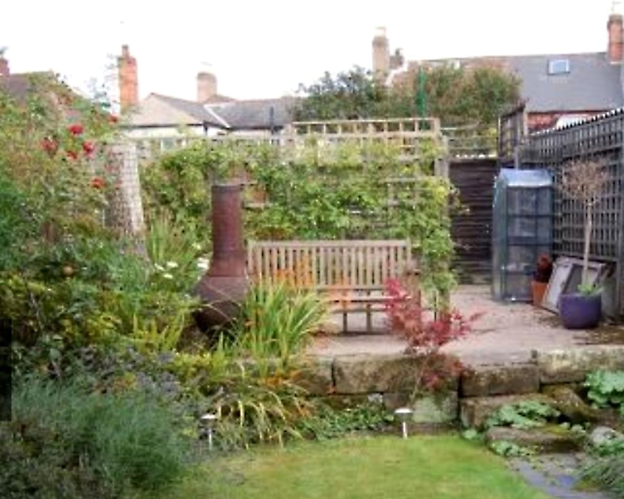 The before shot of a raised stone patio at the bottom of a garden with an old chiminea and trellis fence