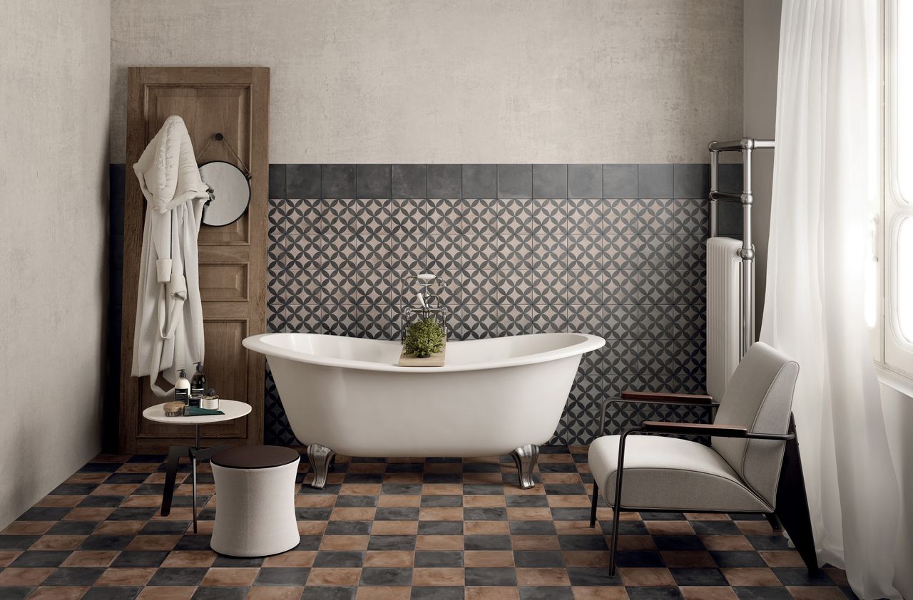 a Moroccan-style bathroom with tiled floor and patterned wall, with a huge white free-standing tub, a gray chair and a wooden door with a robe hung over the back