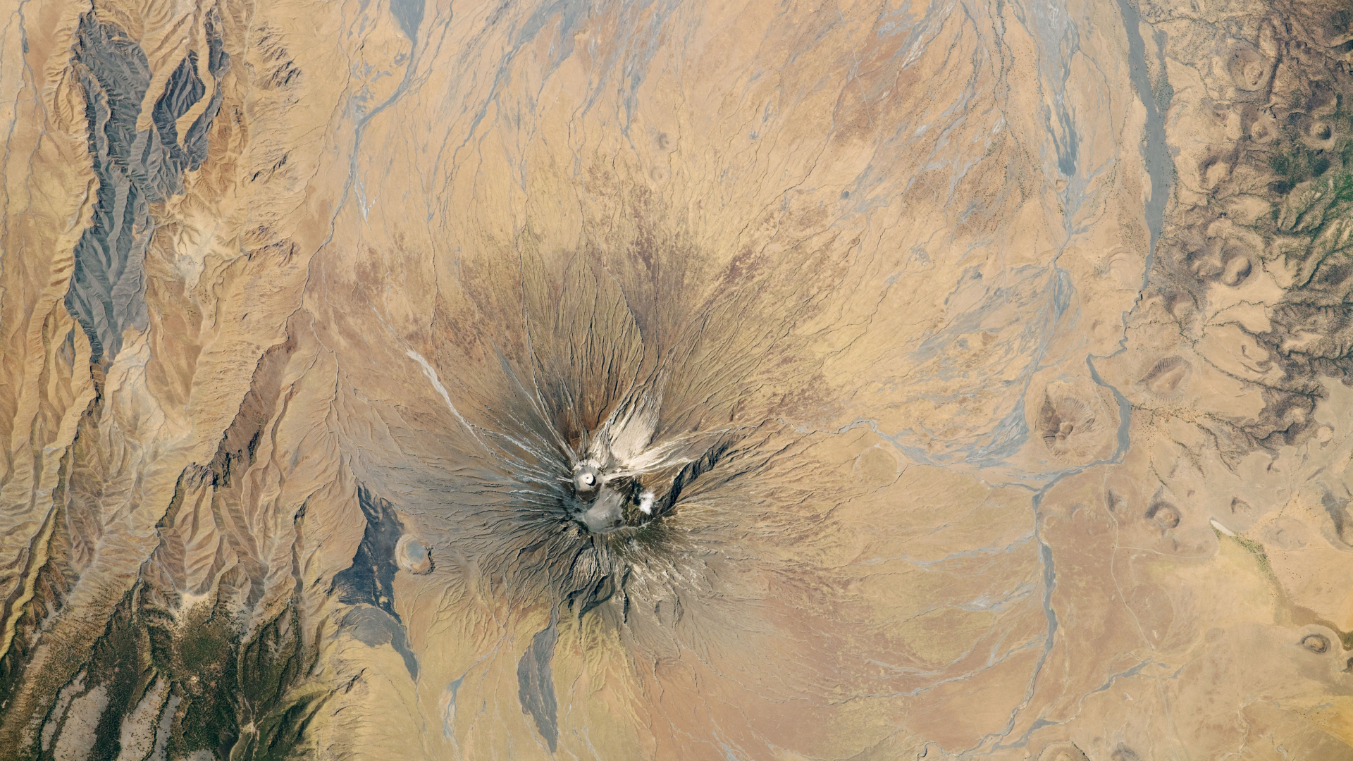 Satellite picture of a dry region with a volcano capped with white ash