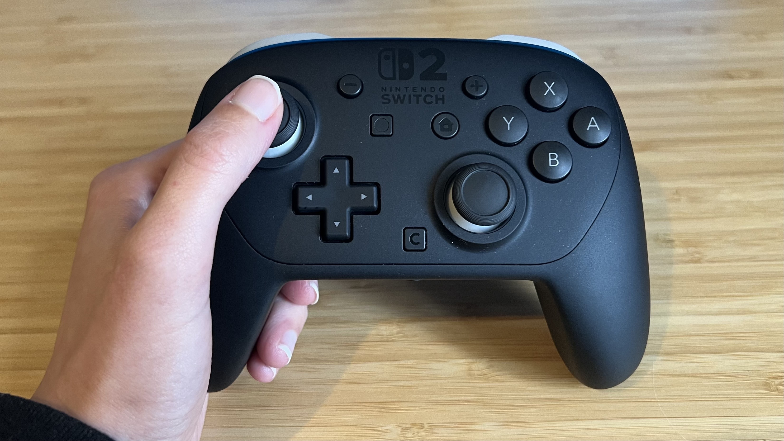 Hand holding Nintendo Switch 2 Pro Controller with thumb on thumbstick