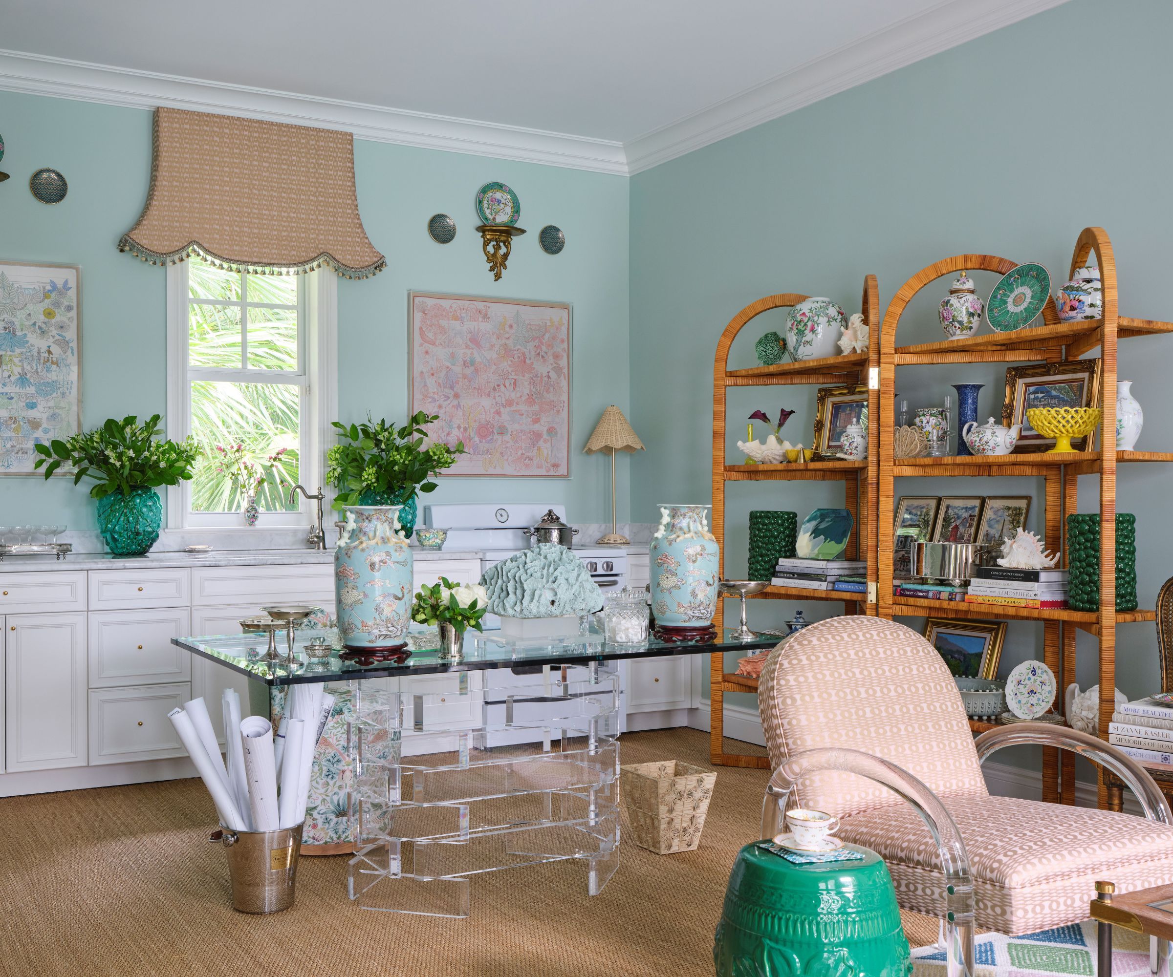 Home office with jute carpet, lucite table, wood shelving, antique vases, and trinkets and teal walls