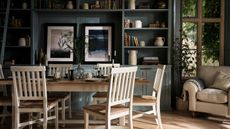 A dining toom with large dark green built in shelves on the back wall beside a window. An upholstered armchair beside it. A white and wood rectangular dining table in front of it with matching chairs surrounding it. 