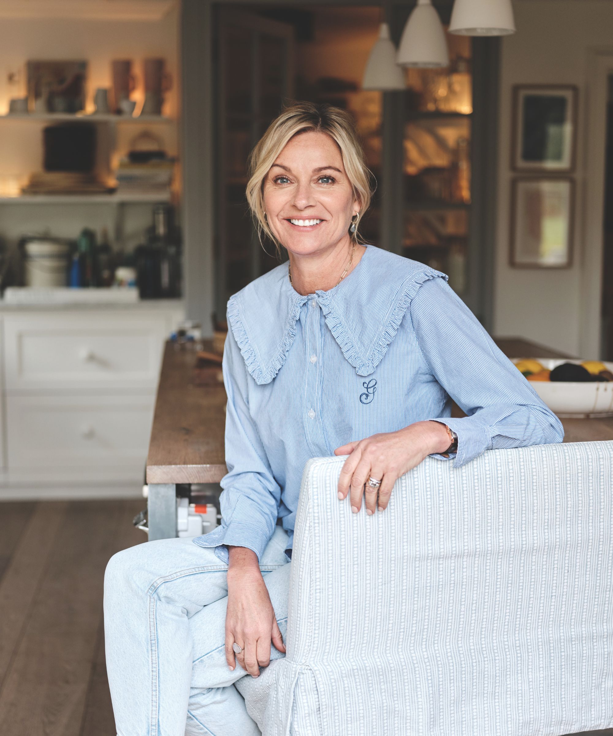 A headshot of a woman in a pale blue blouse sitting on a chair and smiling 