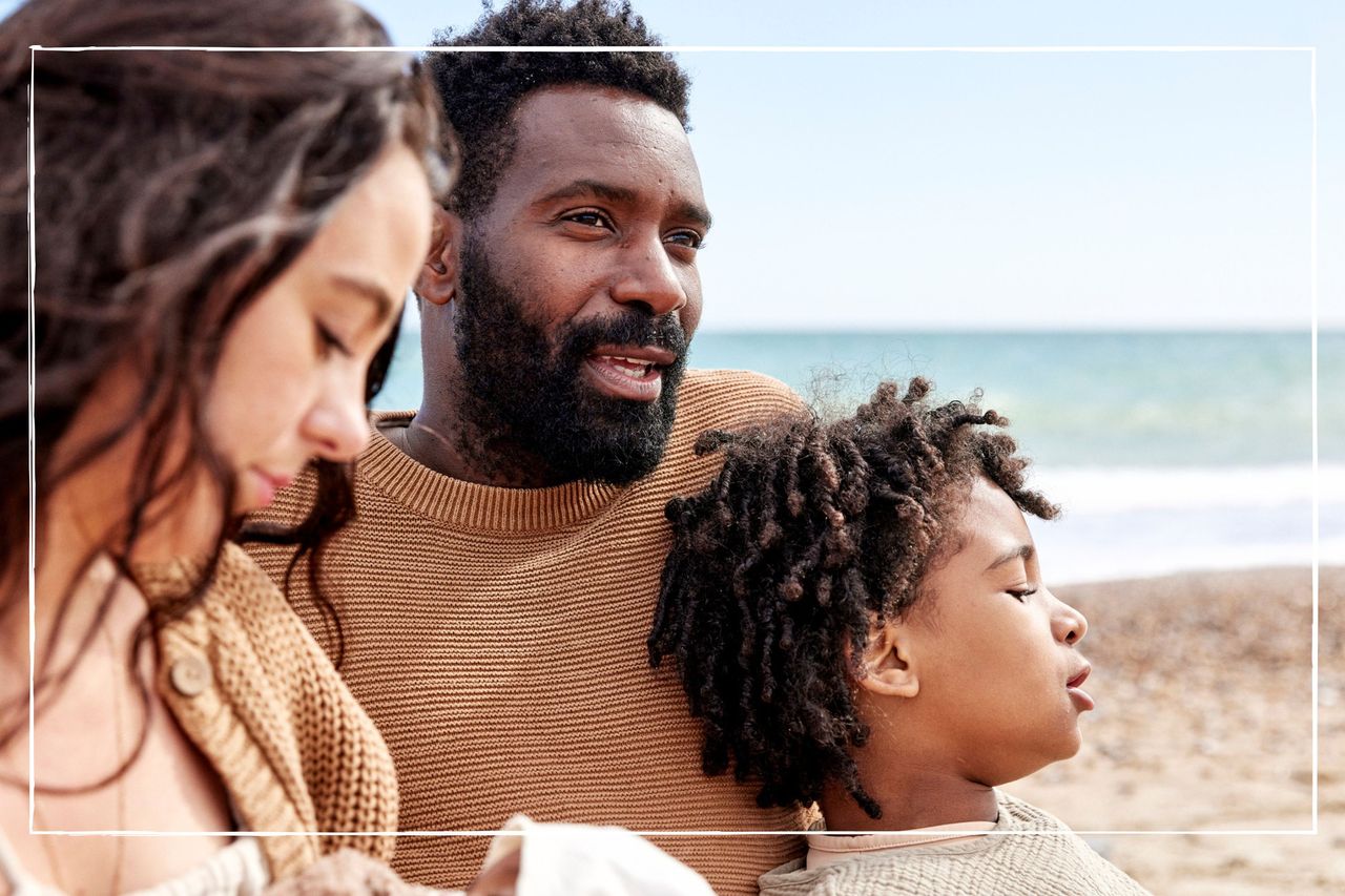 dad looking wistful while sitting on the beach with his partner and two children