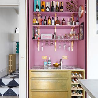 kitchen with pink alcove, pink shelves with glasses and alcohol bottles, with a gold cabinet underneath
