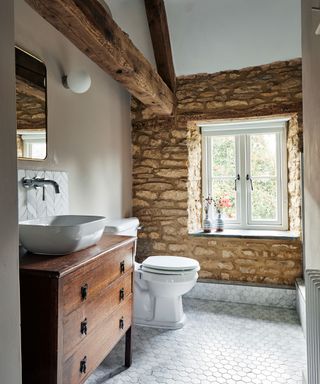 farmhouse bathroom with exposed stone wall and wooden washstand