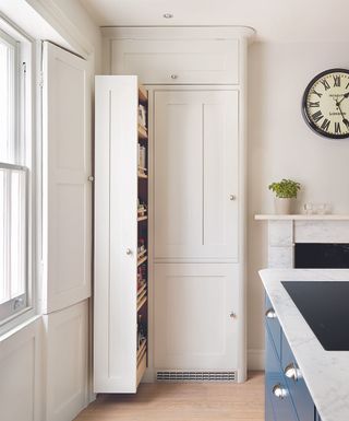A narrow pull out larder in a traditional white kitchen with a large clock on the wall