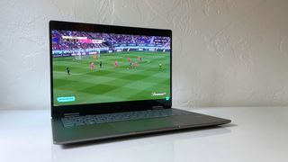 The HP Envy x360 2-in-1 on a white desk with an NWSL game on screen