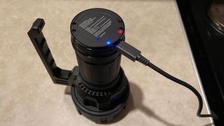 The Acebeam X75 on a table, charging via USB-C and displaying the charging indicator light