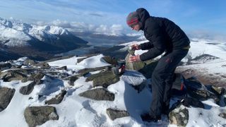 A hiker brews coffee on a snowy summit