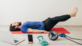 Man performs leg lowers with assorted exercise equipment on the floor around him