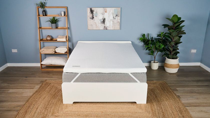 The Helix Dual Comfort Mattress Topper placed top of a grey bed on a white frame in a light blue bedroom with neutral-colored decor. 