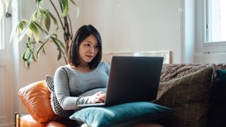 A young pregnant businesswoman sits on a couch, looking at a laptop