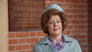Annabelle Apsion as Violet Buckle in a blue hat and coat stands outside the council offices in Call the Midwife.