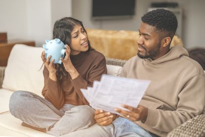 A young couple review their pension arrangements. One holds a piggy bank close to their ear, while the other looks at printed documents (image: Getty Images)