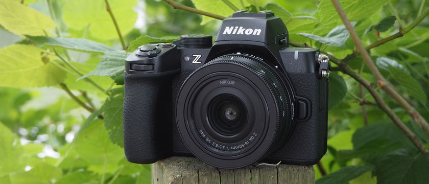 The Nikon Z50 II on a fence post with foliage in the background.