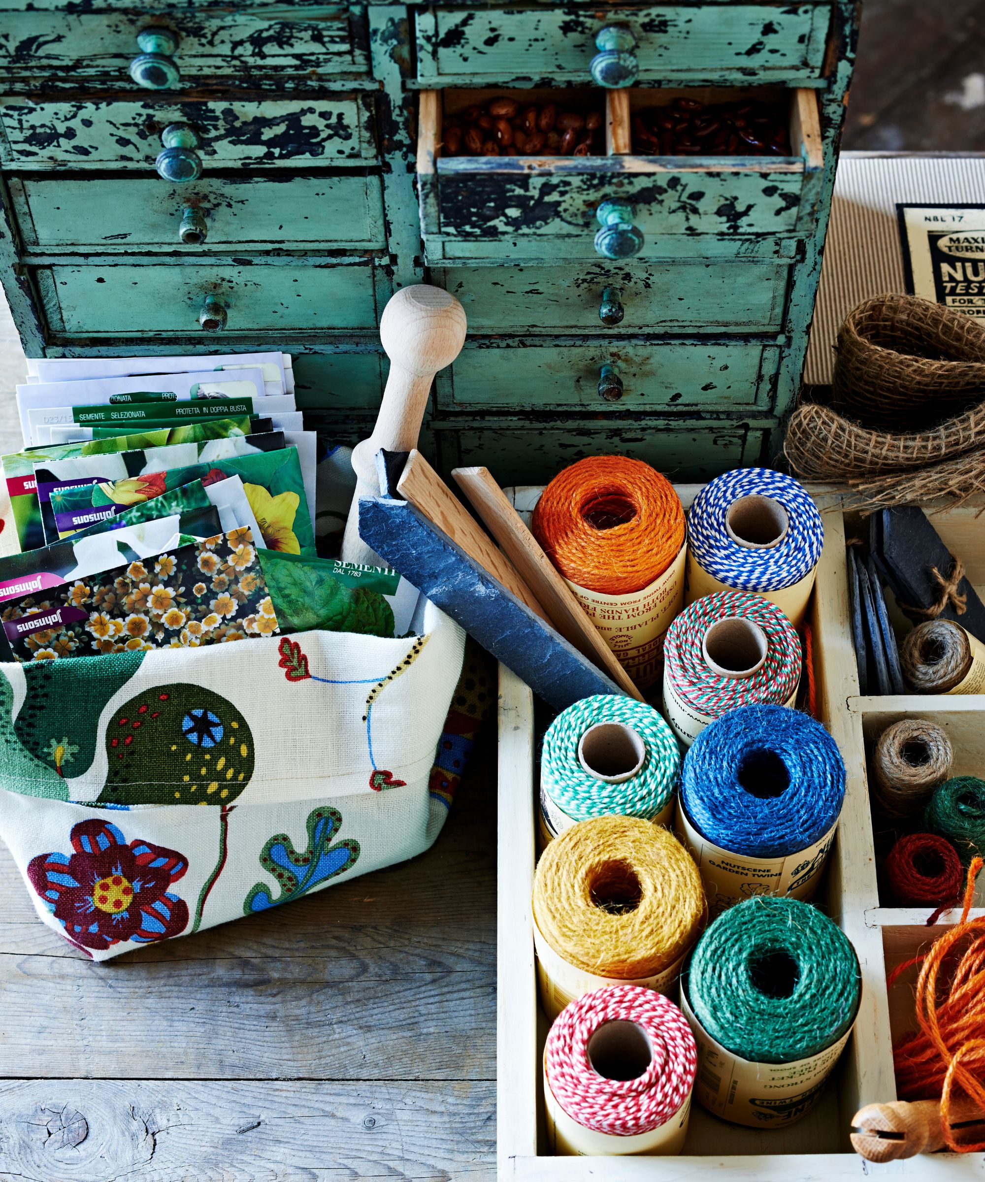 Green drawers and wooden boxes filled with hobby supplies on wooden panelled flooring.