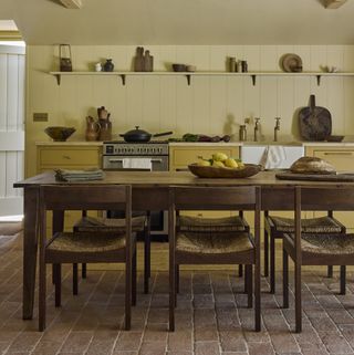 kitchen with large farmhouse table and yellow painted floor units and open shelf in barn conversion with brick paver floor