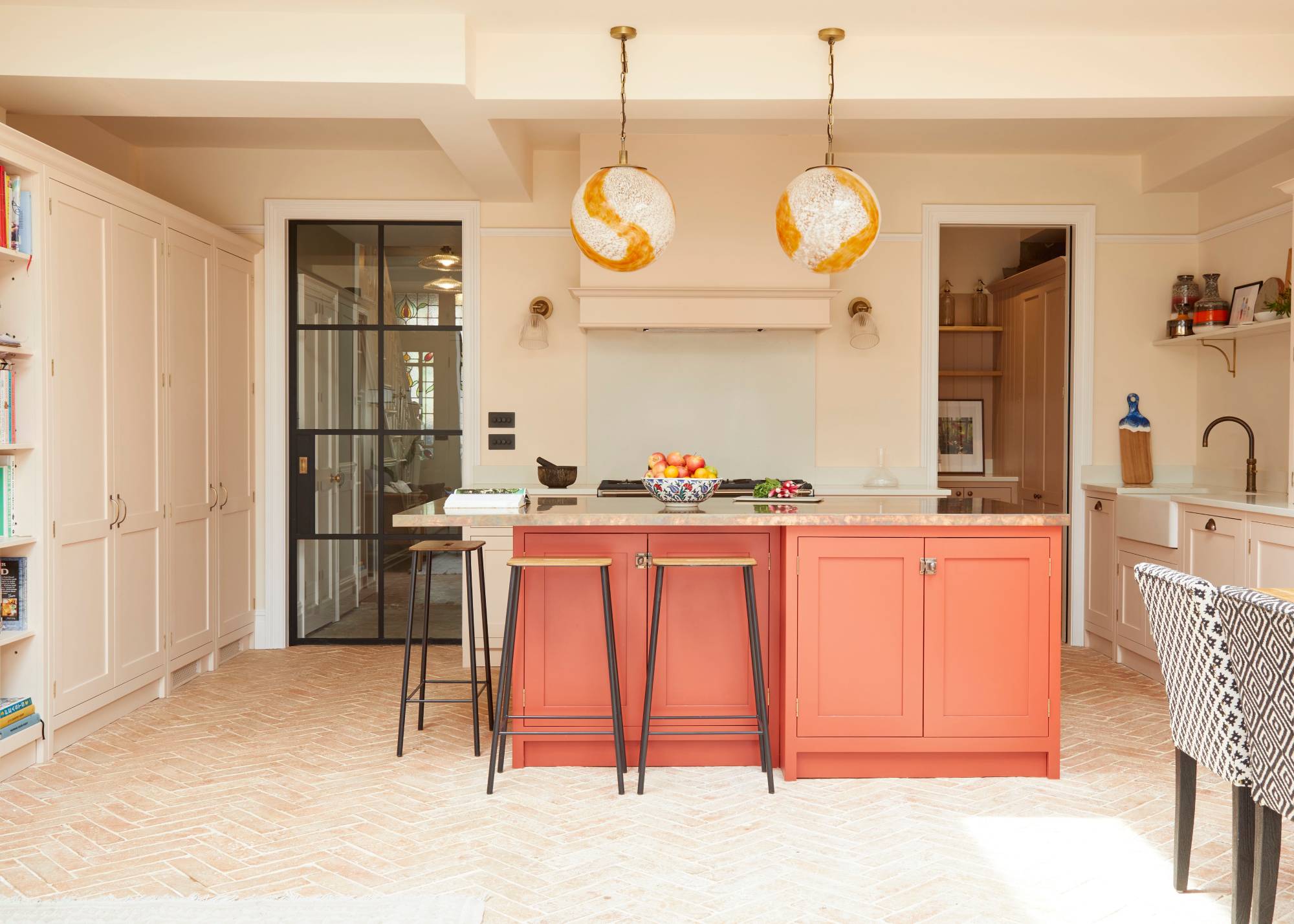 orange kitchen island with seating in white kitchen with tall cupboards and pendant lights