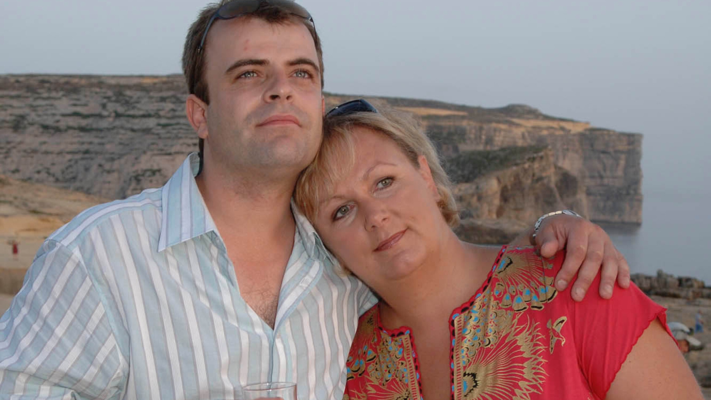 Steve standing with his arm around Eileen's shoulder with a backdrop of some cliffs in Malta.