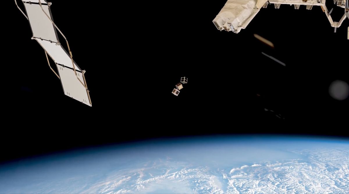 photo showing three small cubical satellites deploying into space from the iss, with earth in the background