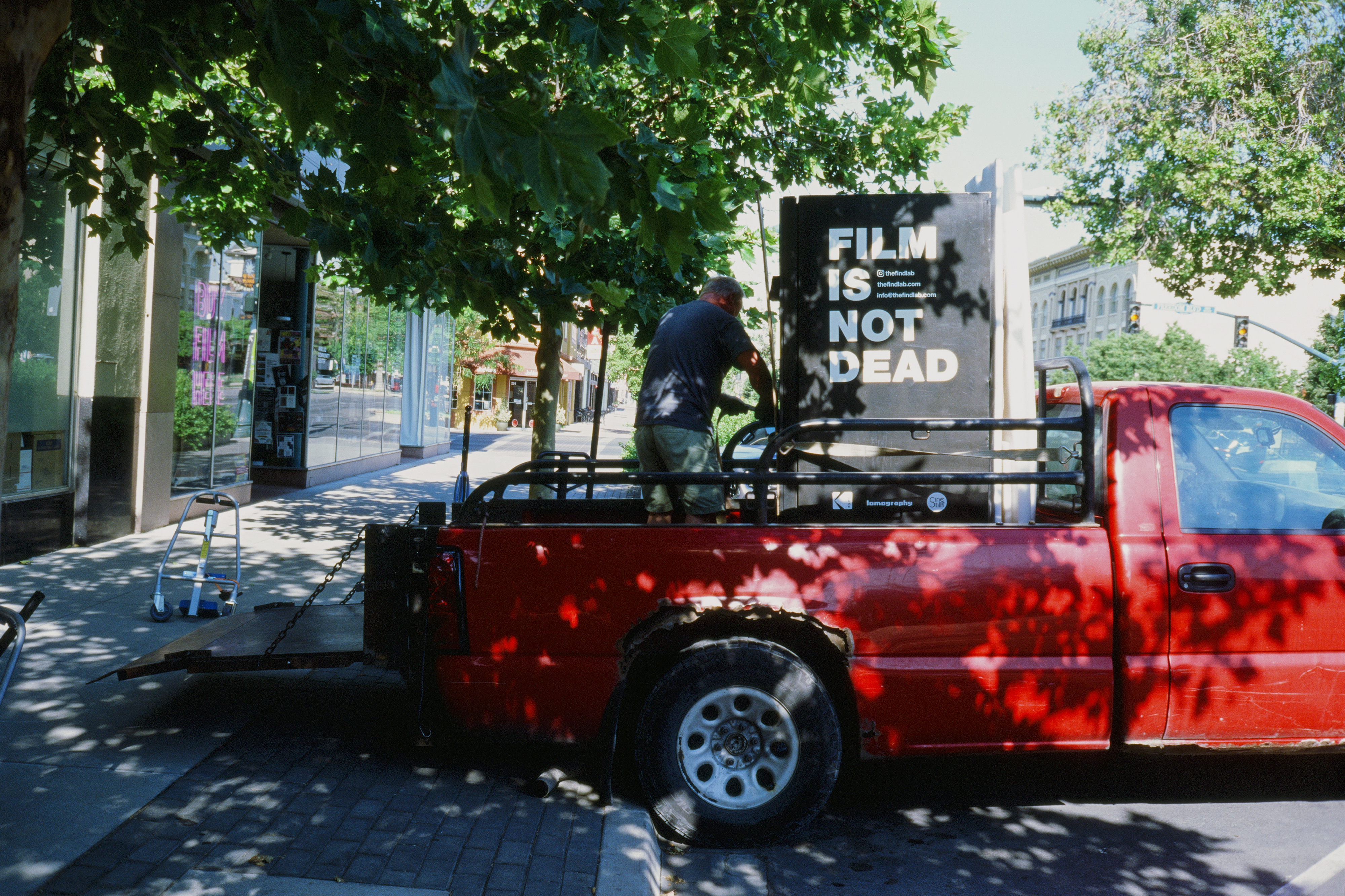 A person loads a film vending machine into the back of a red truck