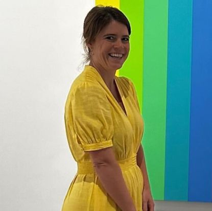 Princess Eugenie wearing a yellow dress and smling in front of a rainbow painting