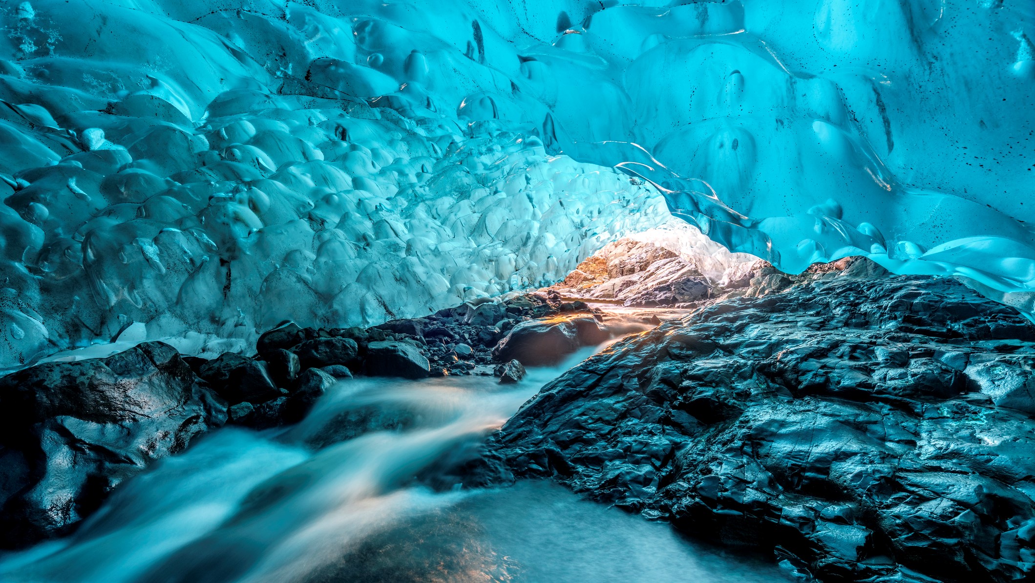 Underneath Vatnajokull glacier in Iceland. The ice cave has water cascading down rocks in the foreground and the walls and roof are made of ice.