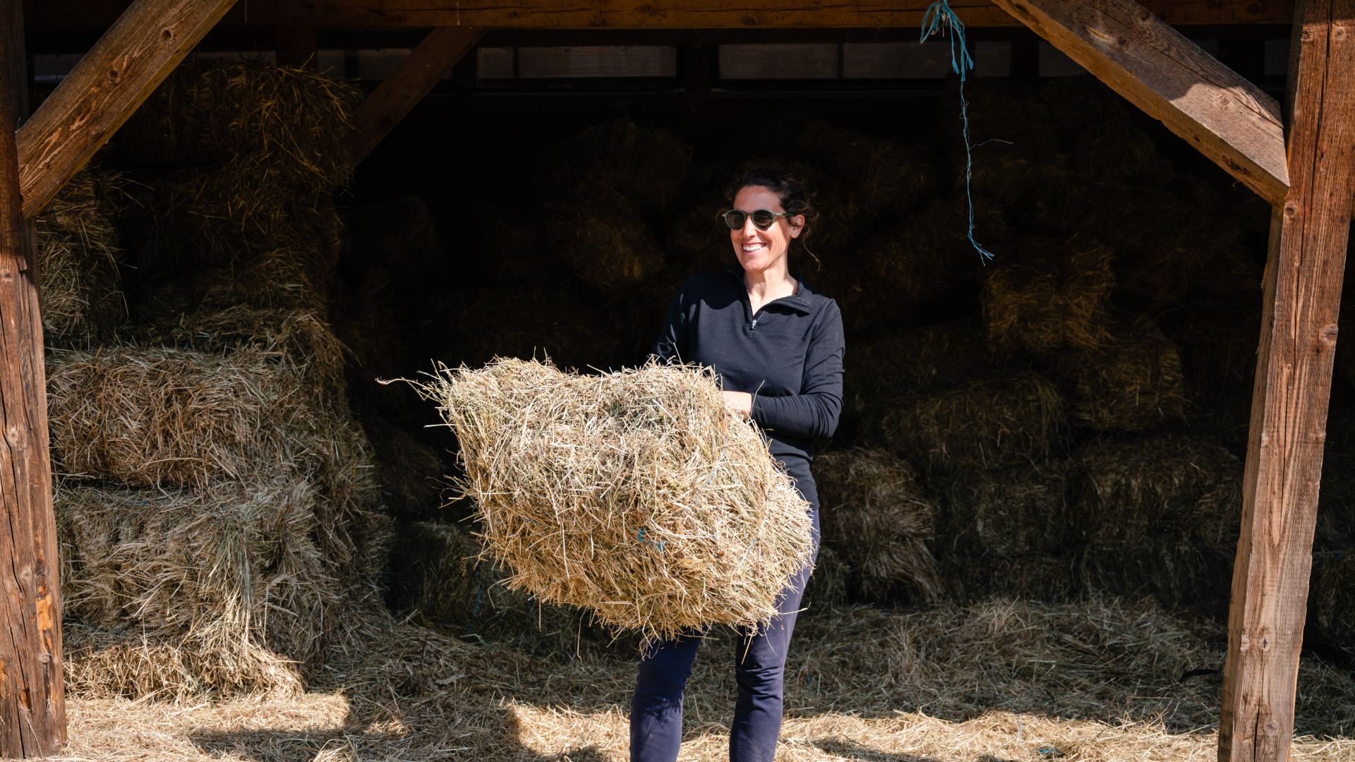 woman carrying a bale of hay away from wooden bale store