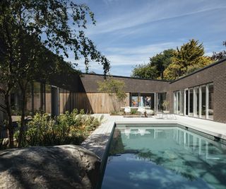 A contemporary courtyard area with pool and garden seating with shade offered by a nearby tree