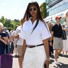 Sabrina Elba wears a pair of white jeans with a white short sleeve shirt, brown belt and brown sandals at Wimbledon in 2025