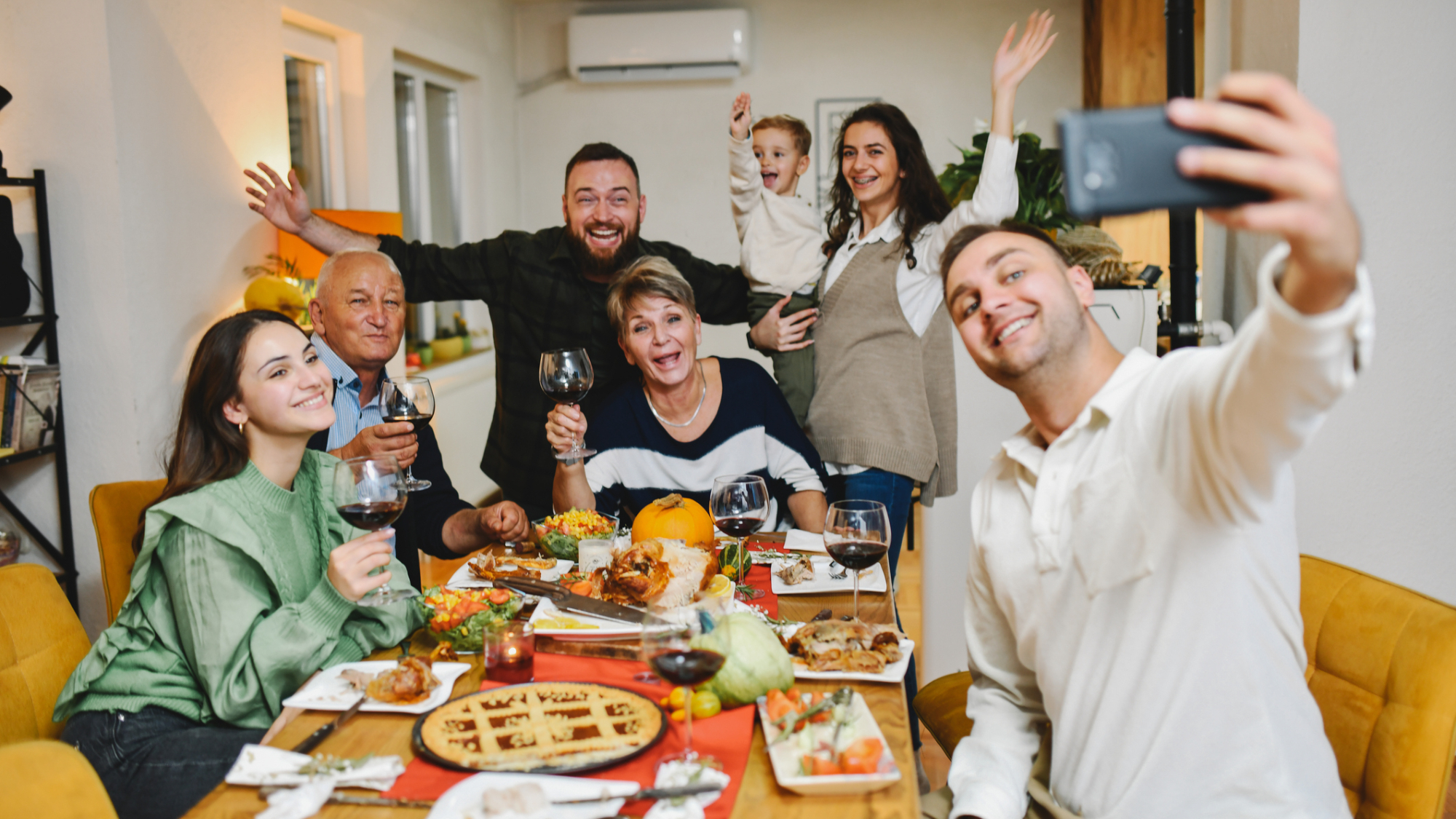 A family, sat around a dinner table, taking a selfie