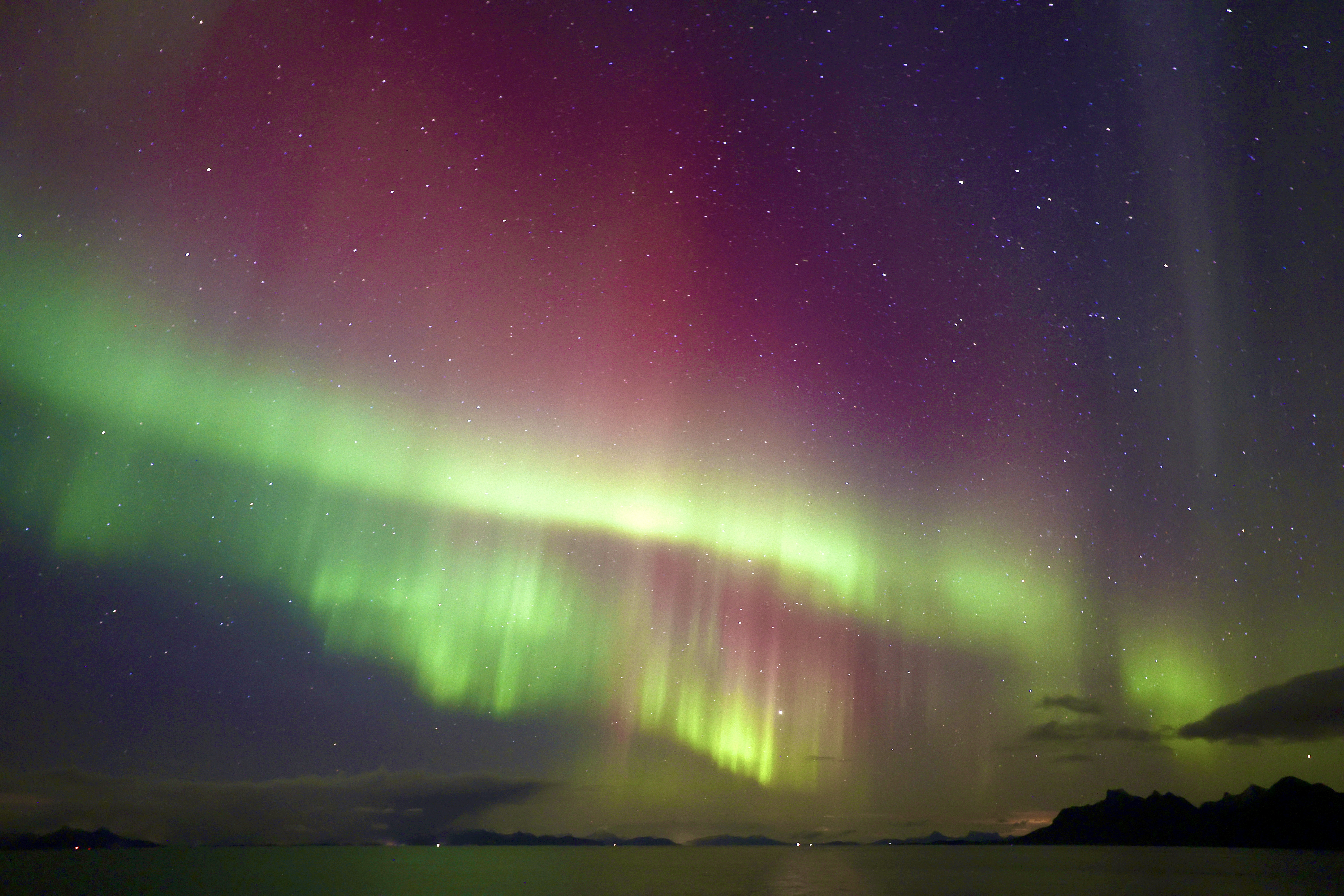 sweeping green and magenta northern lights appear as ribbons in the sky reflected in the water below