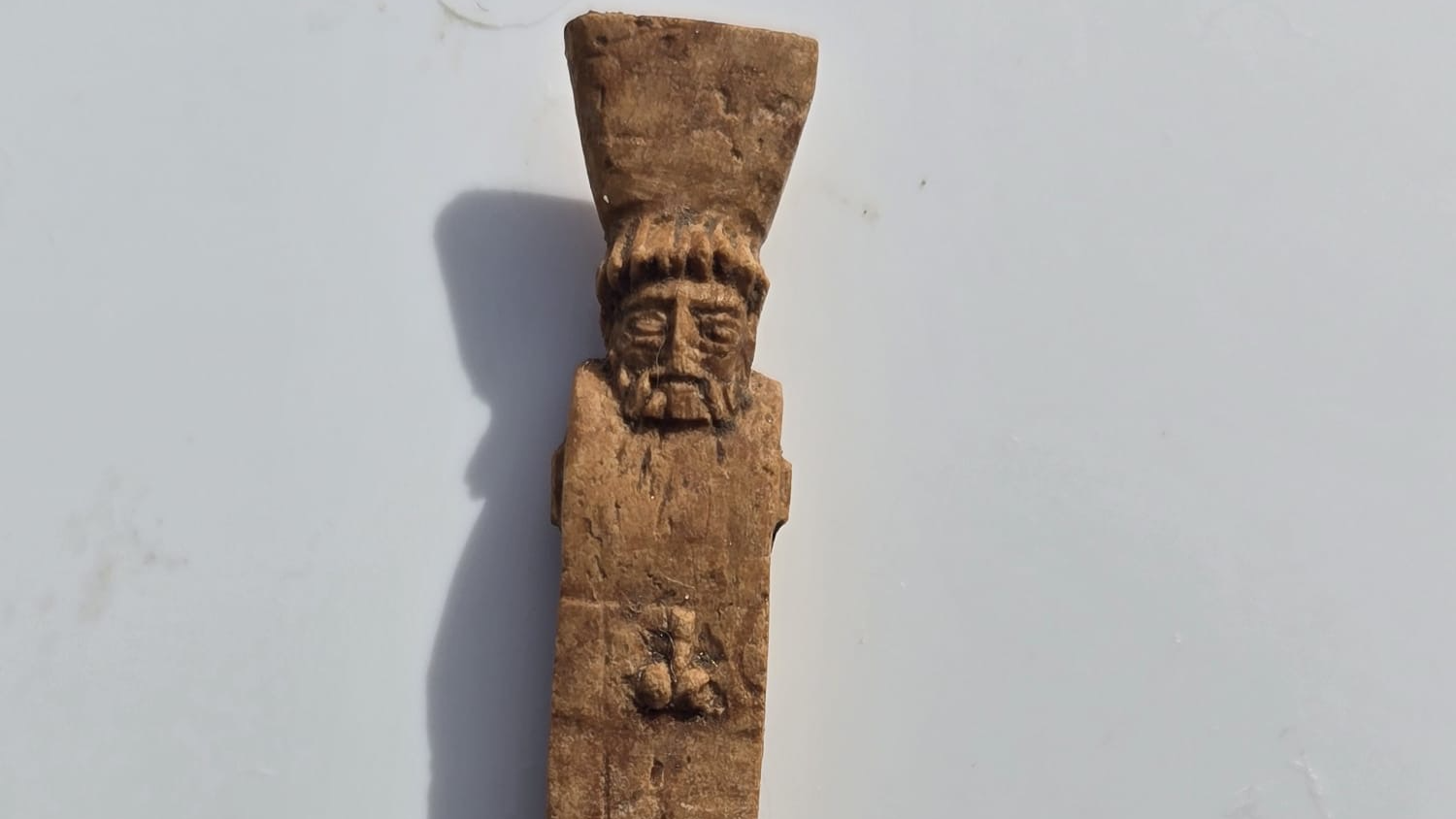 close-up of a bone stylus carved to look like Dionysus with a phallus