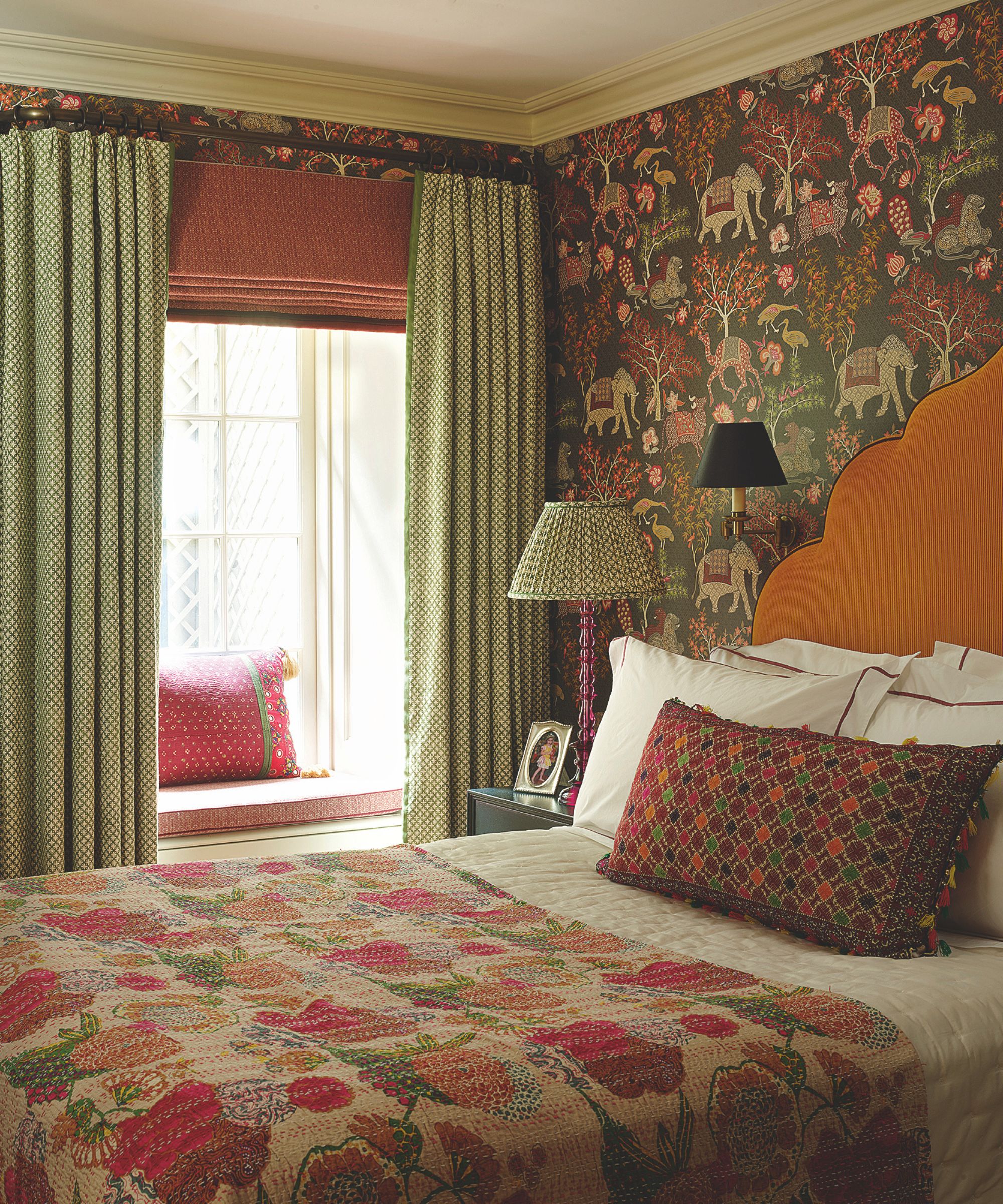 Bedroom with patterned wallpaper featuring animals and trees, orange headboard, green curtains, and a colorful floral quilt