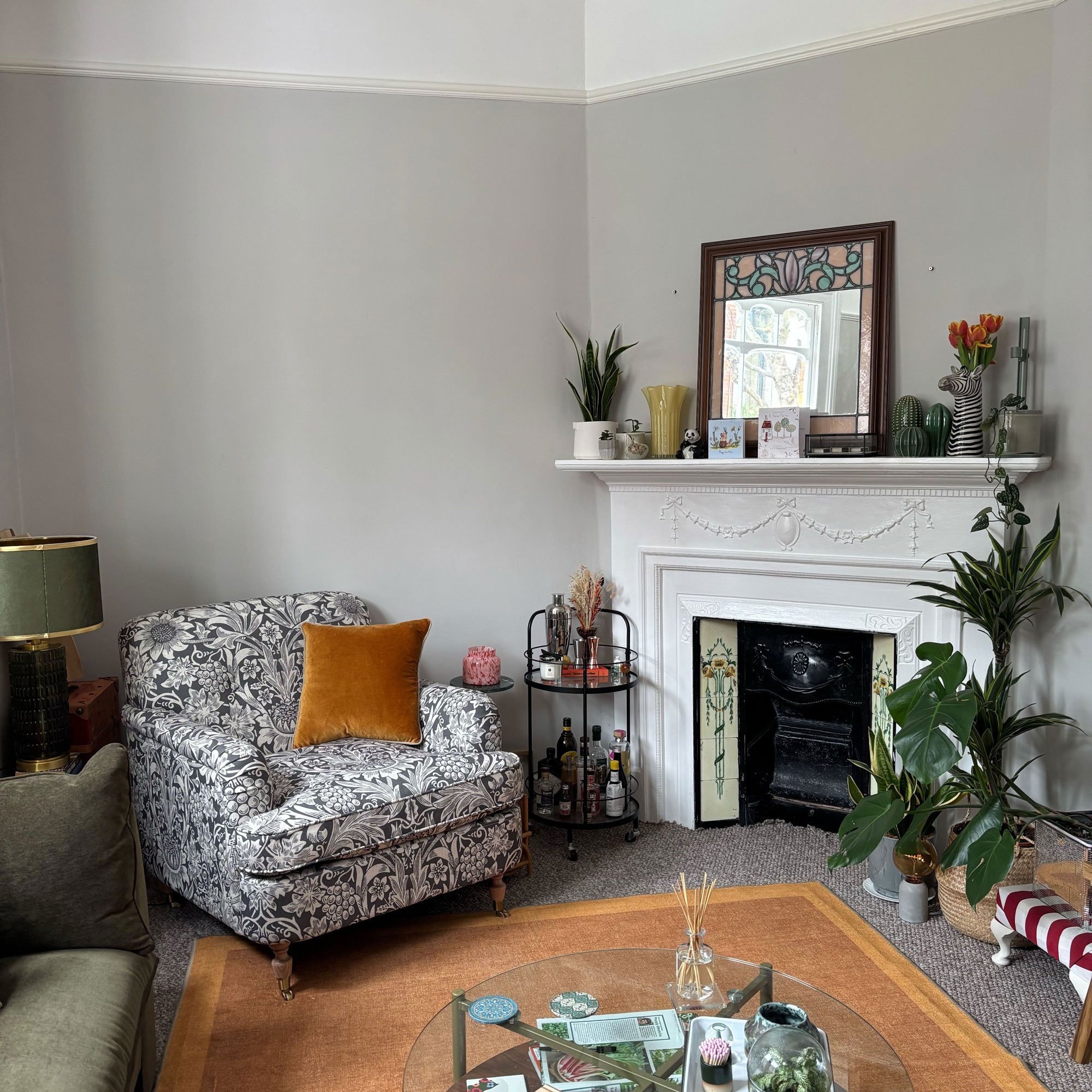Plaster pink living room with a grey and white patterned armchair, white picture rail and moss green sofa.
