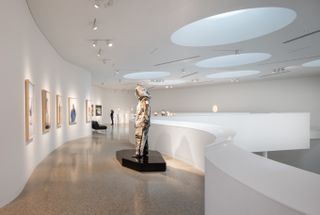 Viewing gallery, white curved walls with framed artwork, mannequin on black gloss stand, circular ceiling lights, neutral marble floor