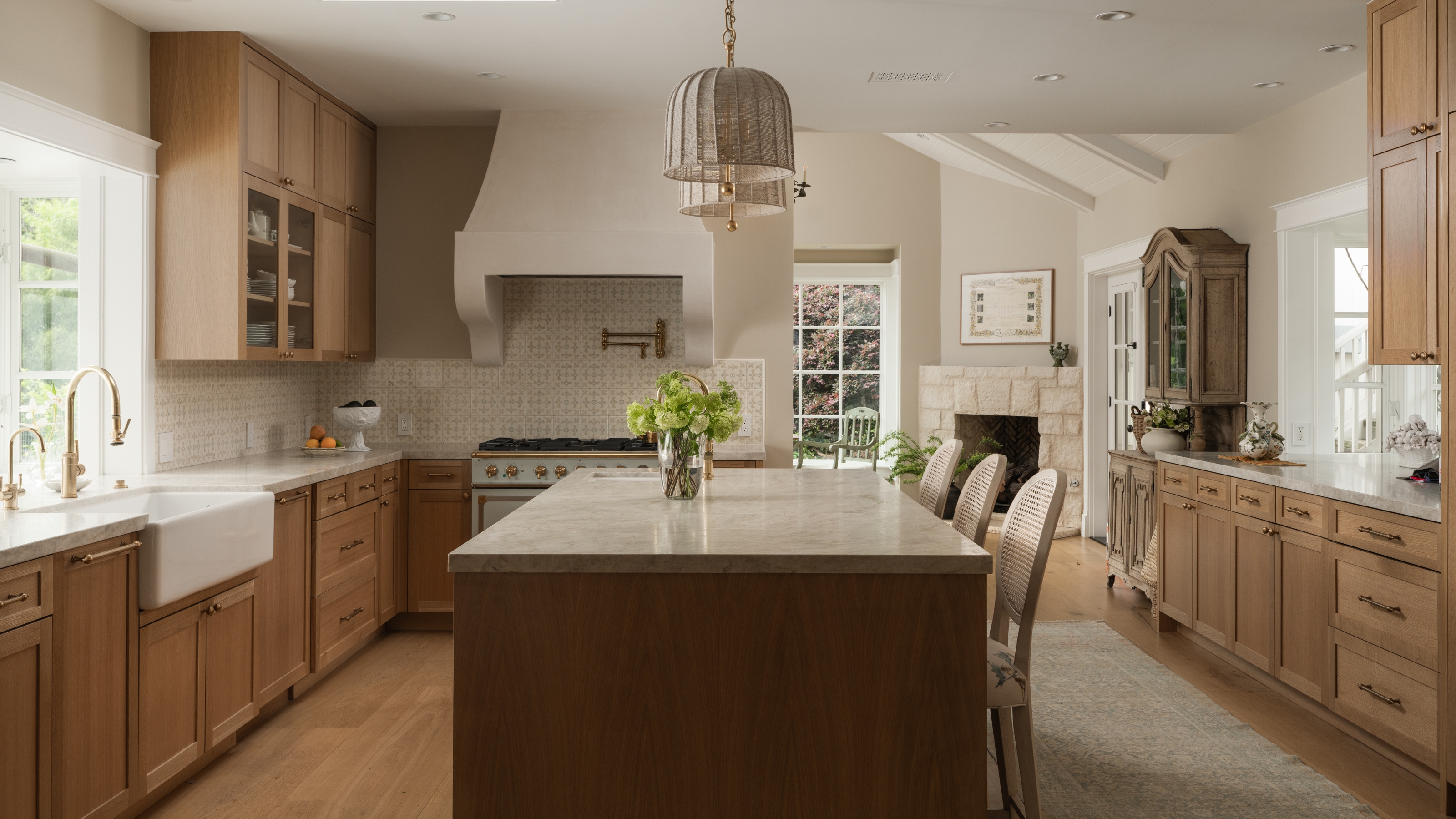 A large kitchen with mid-tone wood cabinets, light wood flooring, and a dark wood island