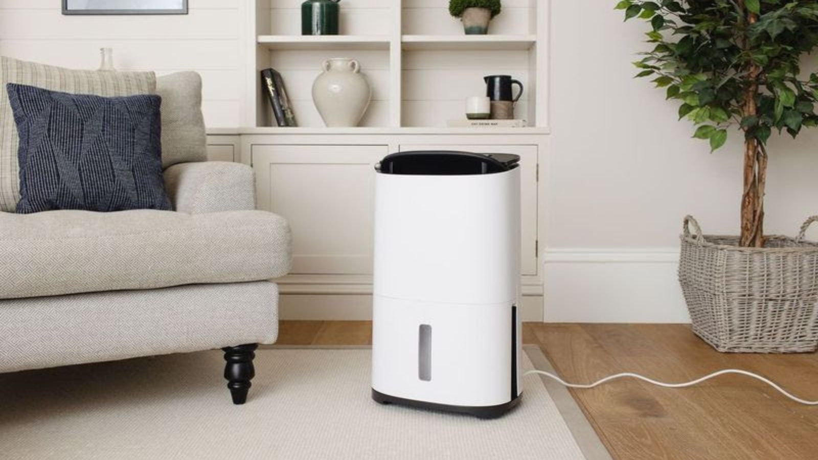 A compact white dehumidifier sits neatly beside a sofa, blending easily into a calm living room setting. Designed to reduce excess moisture, it helps create a more comfortable space while supporting better air quality and minimising dust.