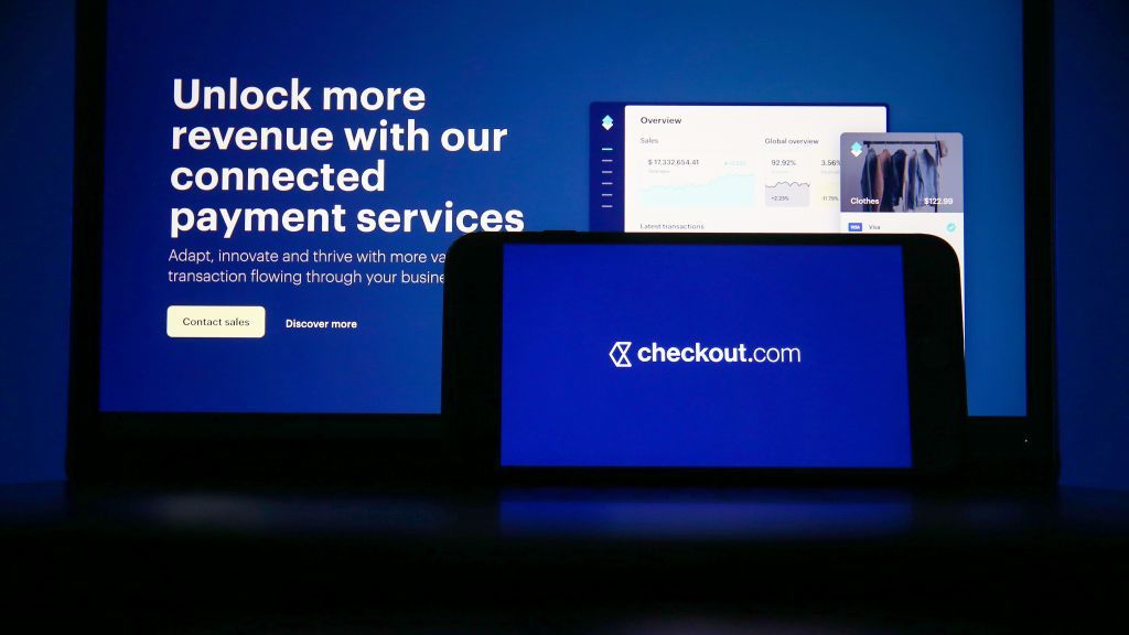 A Checkout.com logo on a laptop computer and mobile phone