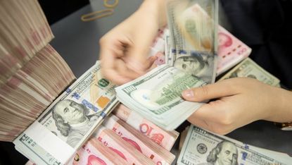 A Chinese bank employee counts 100-yuan notes and US dollar bills at a bank counter.