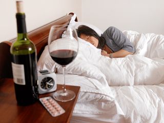 A woman lying in bed next to a bottle of red wine
