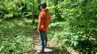 Woman on path in woods wearing waterproof jacket and cycling helmet