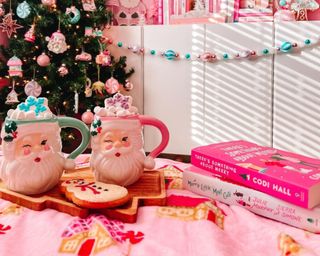 pink living room christmas decor including a blanket, tree, books, and santa mugs