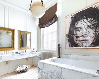 White bathroom with bold artwork, white bath, two antique mirrors, marble bath and sink